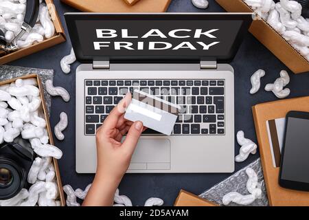 Black Friday e vendita in grande negozio di elettronica concetto. Mano femminile che tiene una carta di credito e lo shopping online attraverso il computer portatile. Il computer è circondato b Foto Stock