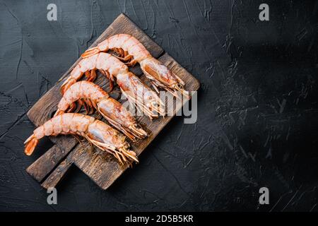 Gamberetti di mare su tagliere di legno su superficie di cemento nero, disposizione piatta con spazio di copia Foto Stock