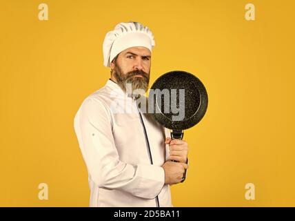 Pentole antiaderenti. Friggere senza olio. utensili professionali. Chef barbuto che prepara la colazione. Padella antiaderente per friggere. Recipienti di cottura smaltati. L'uomo tiene la padella. Pasto frittura. Cibo sano. Foto Stock