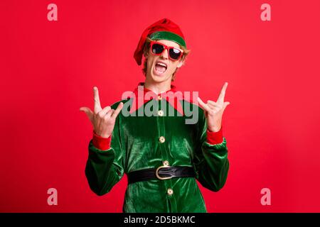 Foto di pazzo funky elfo ragazzo in tendenza sunglass show simbolo delle trombe isolato su sfondo rosso lucido Foto Stock