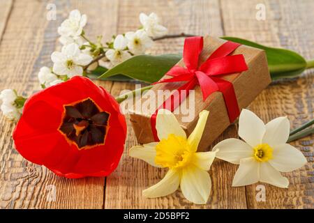 Scatola regalo decorata con un fiore di tulipano, narcisi e gelsomino sulle tavole di legno. Foto Stock