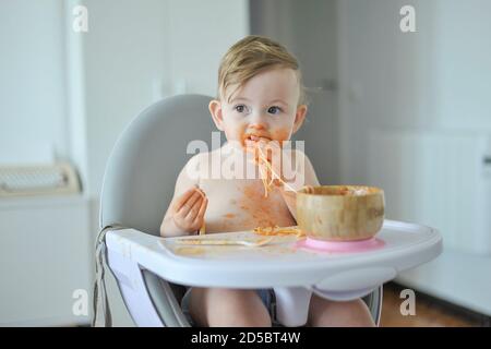 Bambino che mangia la pasta seduto sulla sedia alta Foto Stock