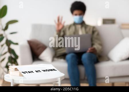 Ragazzo nero teen in maschera medica che studia online su computer portatile, fuoco selettivo di SOGGIORNO A HOME segno, spazio libero Foto Stock