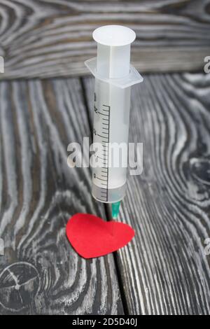 Un cuore di carta forato con una siringa medica. Le tavole di pino sono nere. Foto Stock