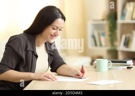 Felice donna che scrive lettera su un tavolo a casa con una luce calda Foto Stock