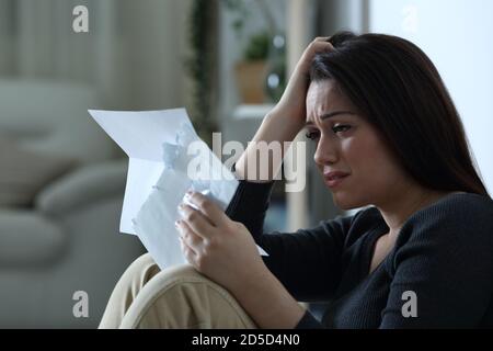 Donna triste che legge una lettera che si lamenta da sola a casa in la notte Foto Stock