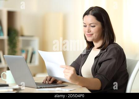 Donna che legge una lettera utilizzando un computer portatile seduto in un tavolo a casa Foto Stock