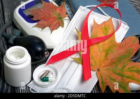 Tonometro per la misurazione della pressione sanguigna. Accanto ad un contenitore con pillole e una maschera medica. Su di loro un nastro è un simbolo della lotta contro l'AIDS. Amo Foto Stock