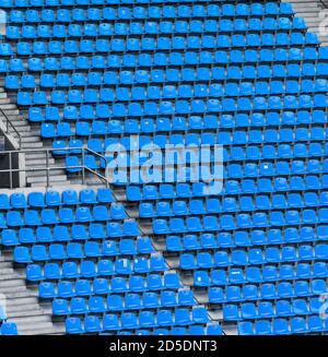 Molte file di posti a sedere blu in un grande stadio sportivo senza spettatori con scale in cemento. Foto Stock