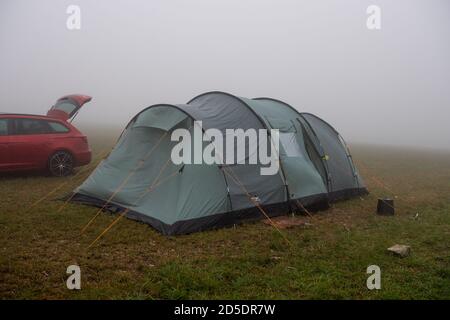 Una tenda singola accanto a un'auto in un campo in cattive condizioni atmosferiche britanniche di nebbia e pioggia che mostra una misera esperienza di campeggio. Foto Stock