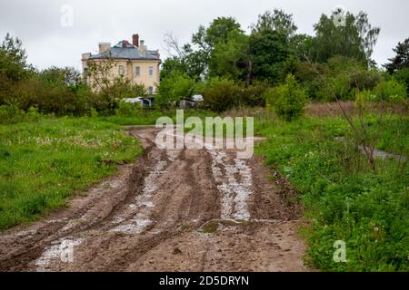 strada di fango di argilla sporca con pozzanghere e cingoli di pneumatici - primo piano con messa a fuoco selettiva e prospettiva lineare Foto Stock