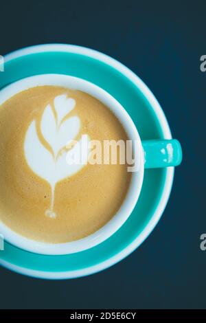 Tazza di caffè in piatto. Tazza di cappuccino italiano fresco Bevanda con disegno floreale su schiuma. Bevanda calda decaffeinata aromatica servita in cerami verde Foto Stock