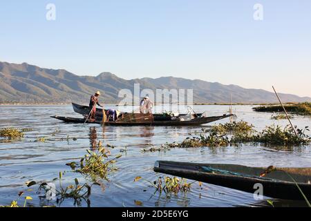 Pescatori locali birmani in piedi su piccole imbarcazioni con metodi tradizionali per catturare il pesce Foto Stock