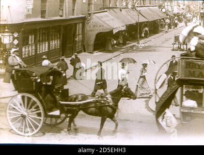 La gente vittoriana viaggia intorno e fa il loro shopping a Londra del diciannovesimo secolo, all'incrocio di St James Street e Oxford Street. Sono visibili le bandiere e i conigli che celebrano l'ottantesimo compleanno della Regina Vittoria. Foto Stock