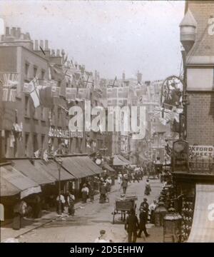 La gente vittoriana viaggia intorno e fa il loro shopping a Londra del diciannovesimo secolo, all'incrocio di St James Street e Oxford Street. Sono visibili le bandiere e i conigli che celebrano l'ottantesimo compleanno della Regina Vittoria. Foto Stock
