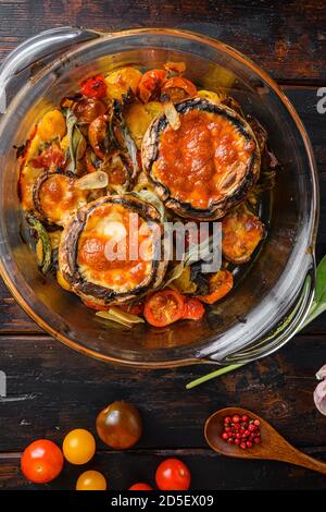 Funghi Portobello, al forno con formaggio cheddar, pomodori ciliegini e salvia in pentola di vetro su vecchio sfondo di legno vista dall'alto. Foto Stock