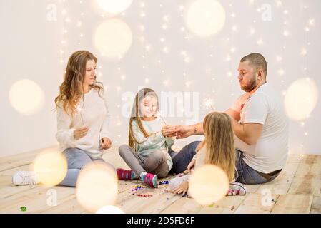 Felici sparklers di luce della famiglia, si divertono, si ingannano intorno sullo sfondo di ghirlande gialle di luci e rami di albero di Natale bokeh. Buono anno nuovo sp Foto Stock