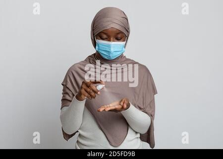 Coronavirus igiene. Madonna musulmana nera in maschera protettiva utilizzando spray disinfettante medico Foto Stock
