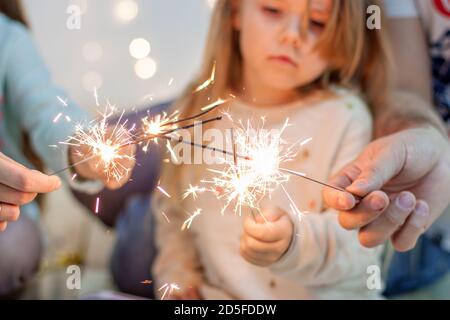 Felici sparklers di luce della famiglia, si divertono, si ingannano intorno sullo sfondo di ghirlande gialle di luci e rami di albero di Natale bokeh. Buono anno nuovo sp Foto Stock