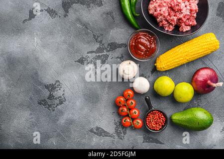 Carne tritata grezza biologica per cucina messicana con ingredienti in ciotola nera, sfondo grigio testurizzato, vista dall'alto con spazio per il testo. Foto Stock