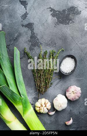 Gambi di porro con erbe ingredienti per cucinare porri brasati, su tavola grigia testurizzata vista dall'alto. Foto Stock