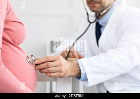 Medico esperto maturo che esamina una giovane donna incinta Foto Stock