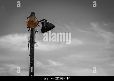 Vecchia lampada elettrica in metallo arrugginito su lampione in cemento - immagine in bianco e nero con colore selezionato e luce di copia Foto Stock