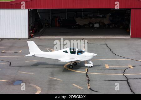 Un aereo sportivo vicino ad un hangar aperto in cui ci è un piccolo elicottero Foto Stock