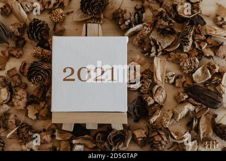 2021 scritto in marrone sulla tela di un cavalletto con frutti marroni secchi e fiori intorno ad esso. Foto Stock