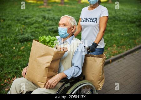 Maschio più anziano in maschera medica che tiene la borsa della spesa di carta sopra le gambe Foto Stock