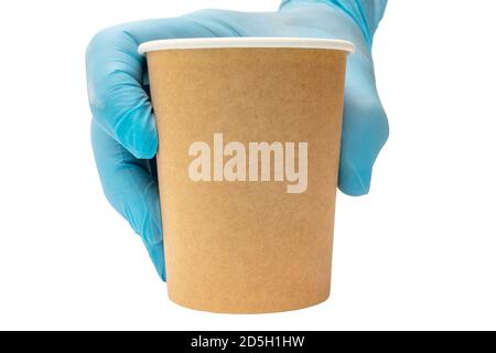 Una tazza di caffè di carta marrone in una mano maschile in un guanto medico blu. Foto Stock