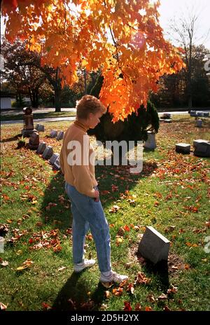 La donna visita un luogo della tomba di una persona amata in un cimitero con albero colorato sullo sfondo Foto Stock