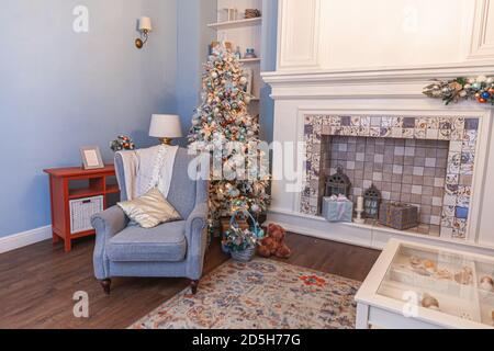 Camera classic decorata con interni natalizi, albero di Capodanno con decorazioni in argento. Moderno appartamento di design moderno in stile classico blu con camino e poltrona. Vigilia di Natale a casa Foto Stock