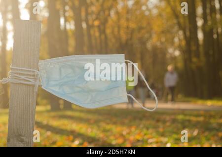 Al tramonto d'autunno, la maschera medica usa e getta pende in un parco pubblico. Inquinamento plastico causato da Covid 19. Foto Stock