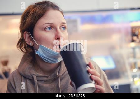 Una giovane donna in un caffè durante la pandemia del coronavirus. La donna beve caffè sulla strada presso i caffè aperti dopo la quarantena del coronavirus Foto Stock