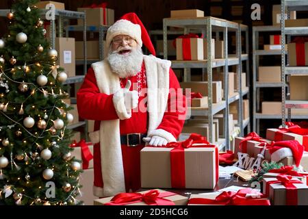 Felice Babbo Natale che indossa un costume che mostra i pollici in piedi in officina. Foto Stock