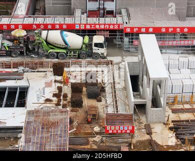 Cantiere urbano con betoniere, calcestruzzo, impalcature, materiali da costruzione, barrette e cartelli scritti in lingua cinese sulla sicurezza dei lavoratori Foto Stock