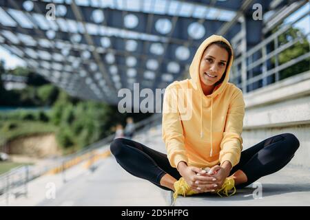 Donna sportiva con cappuccio giallo che si riscalda sulle scale Foto Stock