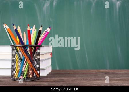 Concetto di istruzione scolastica. Foto ravvicinata di pastelli colorati e una pila di libri di testo isolati sul copyspace verde della lavagna Foto Stock