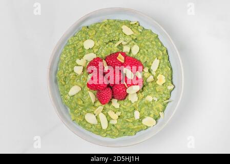 Porridge Matcha con lamponi e noci in una ciotola su sfondo di marmo bianco. Vista dall'alto. Colazione dietetica. Cibo sano Foto Stock