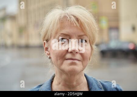 Il volto di una donna bianca matura sullo sfondo di una città piovosa. Foto Stock