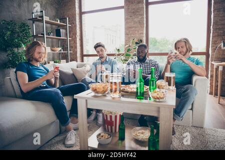 Ritratto di quattro simpatici e attraenti ragazzi che si riunono seduti divan utilizzando il dispositivo digitale trascorrere del tempo libero divertimento in industriale stile loft Foto Stock