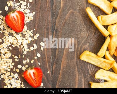 Cibo sano contro malsano e concetto di dieta. Fiocchi di avena e fragole fresche vs patate fritte francesi isolato su legno tavolo studio sfondo wi Foto Stock