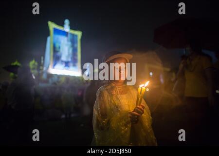 Bangkok, Thailandia. 13 ottobre 2020. Un bambino che indossa un impermeabile per proteggersi dalla pioggia visto tenere candele durante la cerimonia del quarto anniversario che segna la morte del defunto re tailandese Bhumibol Adulyadej (Rama 9). Credit: SOPA Images Limited/Alamy Live News Foto Stock