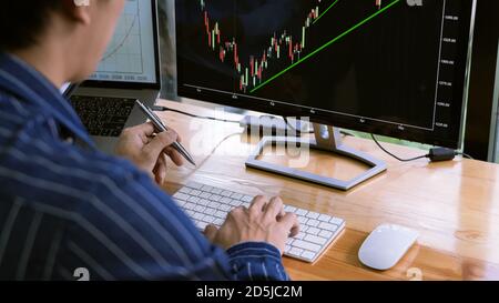 broker mostrando un po 'ascendente al suo collega di pianificazione e analisi grafico delle negoziazioni di borsa con i dati di grafico di borsa su più schermi del computer Foto Stock