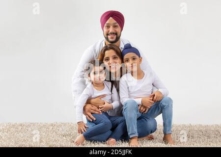 SIKH RAGAZZO E RAGAZZA SEDUTA SUL GREMBO DELLA MADRE E PADRE ABBRACCIANDOLI Foto Stock