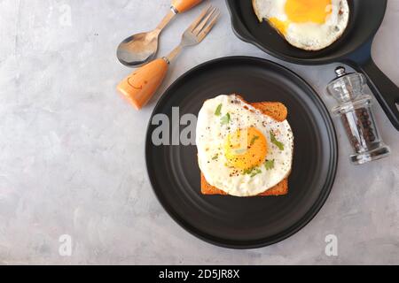 Uovo fritto su pane integrale con sale e pepe per la colazione classica. Uovo soleggiato con pane marrone su piatto nero su tavolo di legno. Foto Stock