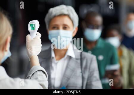 Donna matura in maschera protettiva di prova con attrezzature mediche speciali in aeroporto Foto Stock