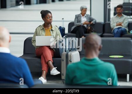 Giovane donna africana seduta e che usa il suo laptop mentre si siede nella sala d'attesa dell'aeroporto Foto Stock