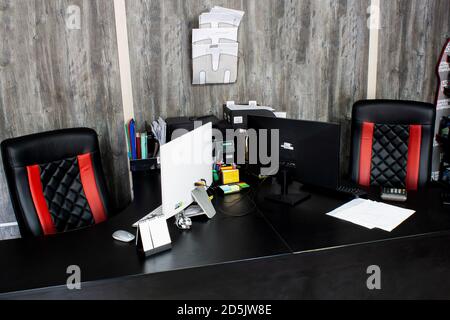 Spazio di lavoro in ufficio con computer. Monitor su tavoli neri con sedie in pelle da regista. Carta, documenti, tastiera, mouse, calcolatrice, stampante, s Foto Stock